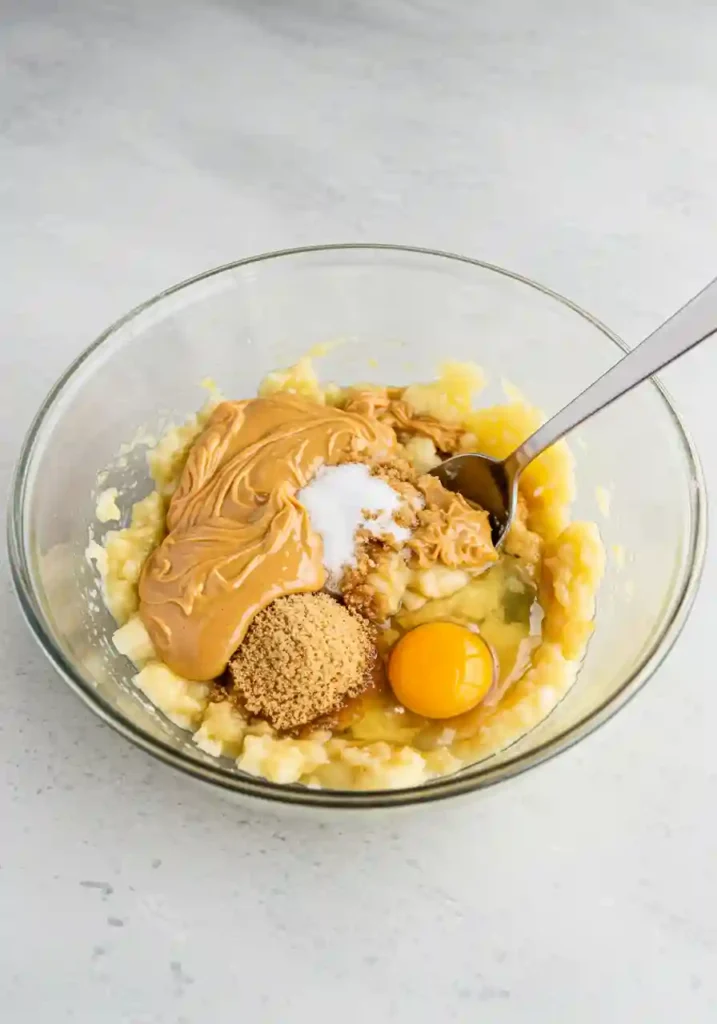 Mixing peanut butter, mashed banana, sugar, and egg in a bowl