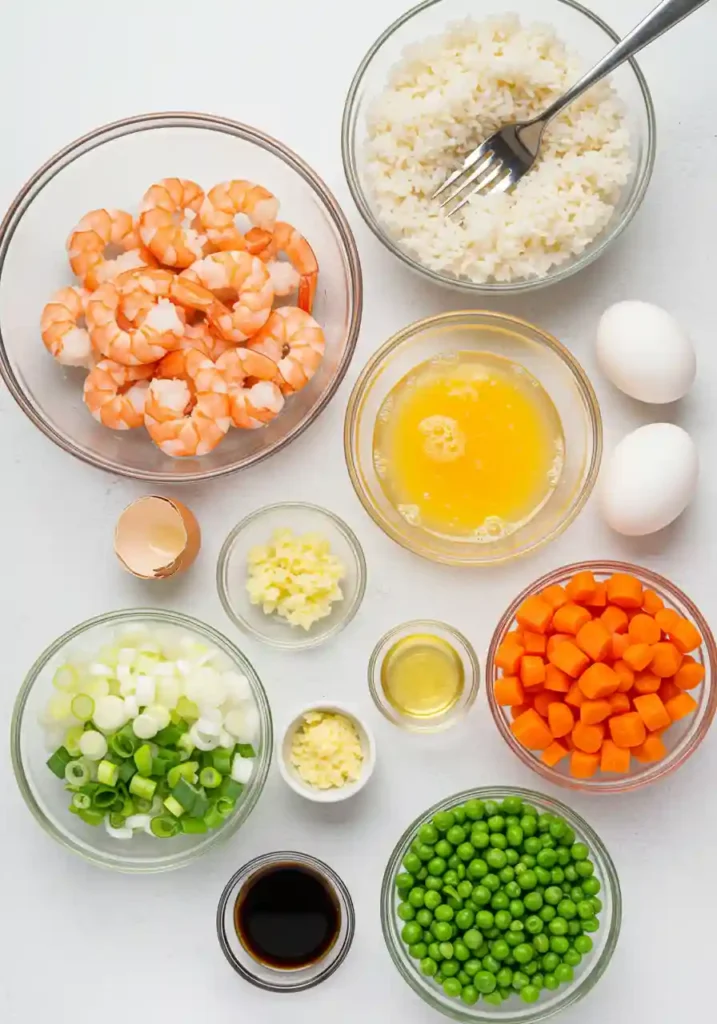 Shrimp, cooked rice, peas, carrots, eggs, and sauces on a board