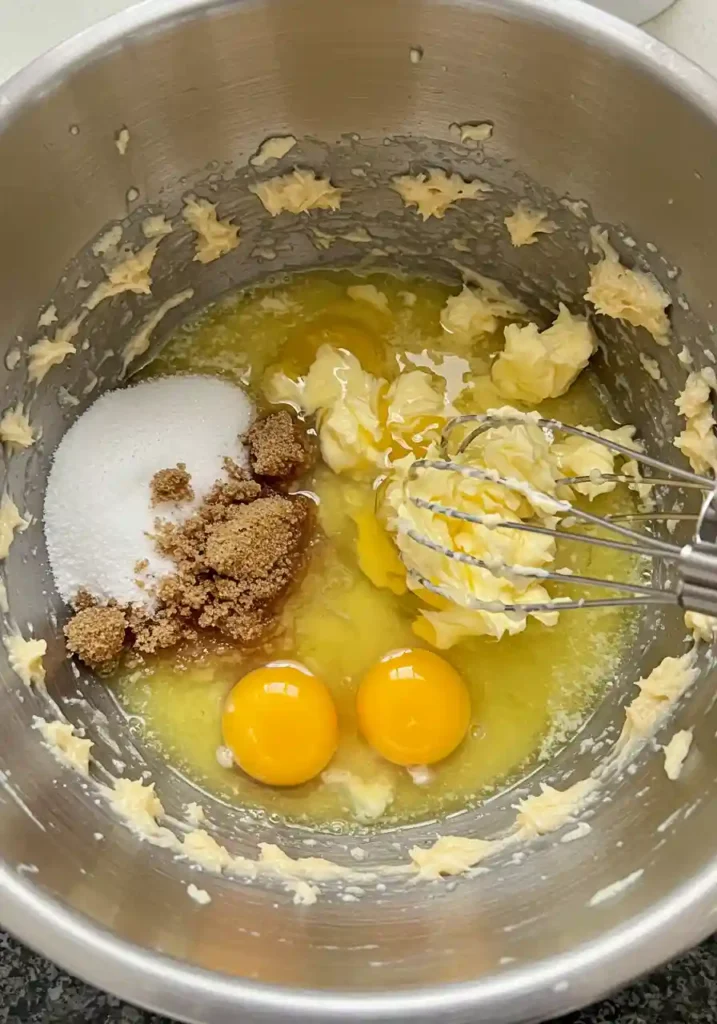 Whisking melted butter, sugars, sour cream, and eggs in a bowl