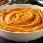 Bowl of sweet potato puree on a wooden table with spoon