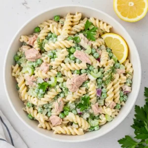 Tuna pasta salad served in a white bowl with lemon wedges and herbs
