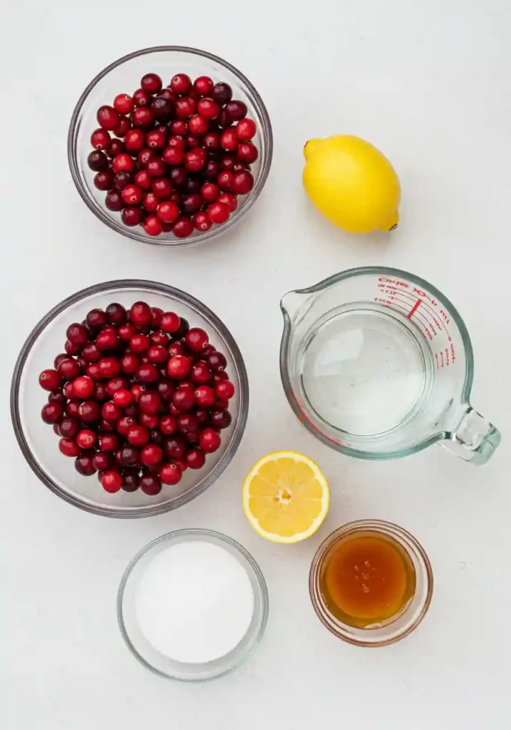 Cranberries, water, lemon, and sugar in bowls on table