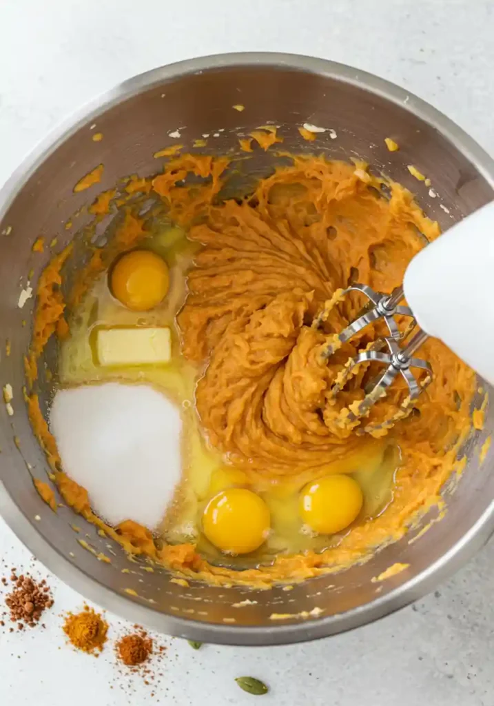 Hand mixer blending sweet potato pie ingredients