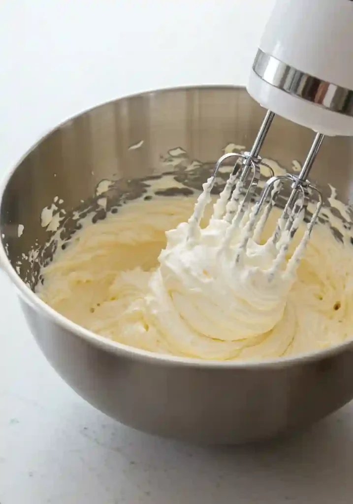 Electric mixer blending smooth cream cheese and whipped cream for cheesecake cups