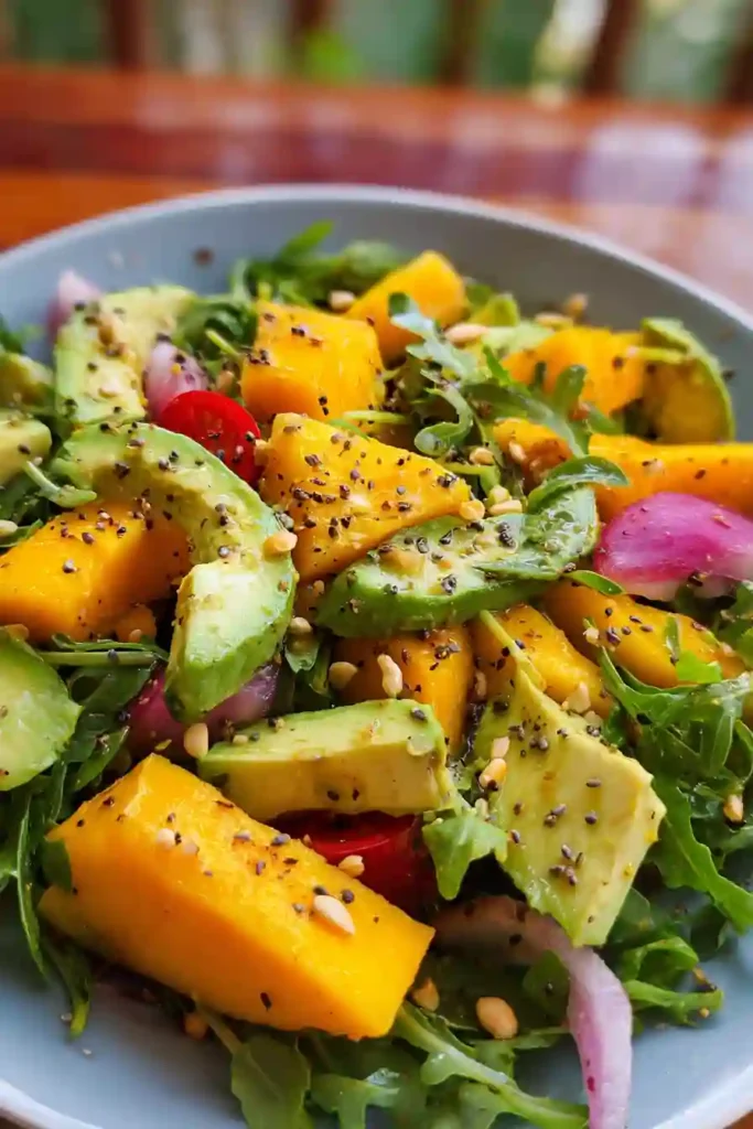 Diced avocado and mango being gently tossed with lime dressing and herbs in large mixing bowl