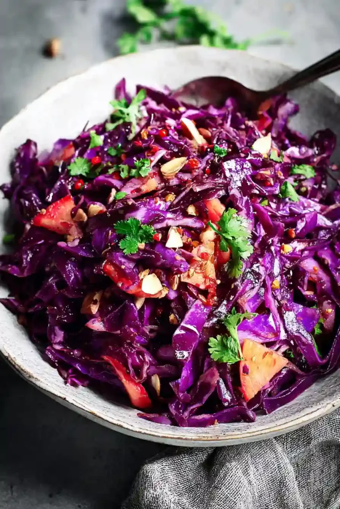 Shredded red cabbage being tossed with carrots, apples and vinaigrette dressing in large mixing bowl