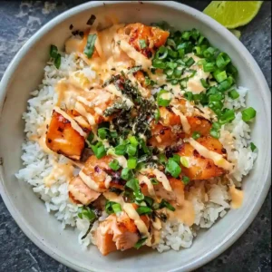 Close-up of assembled salmon bowl with sauce, rice, greens, and toppings