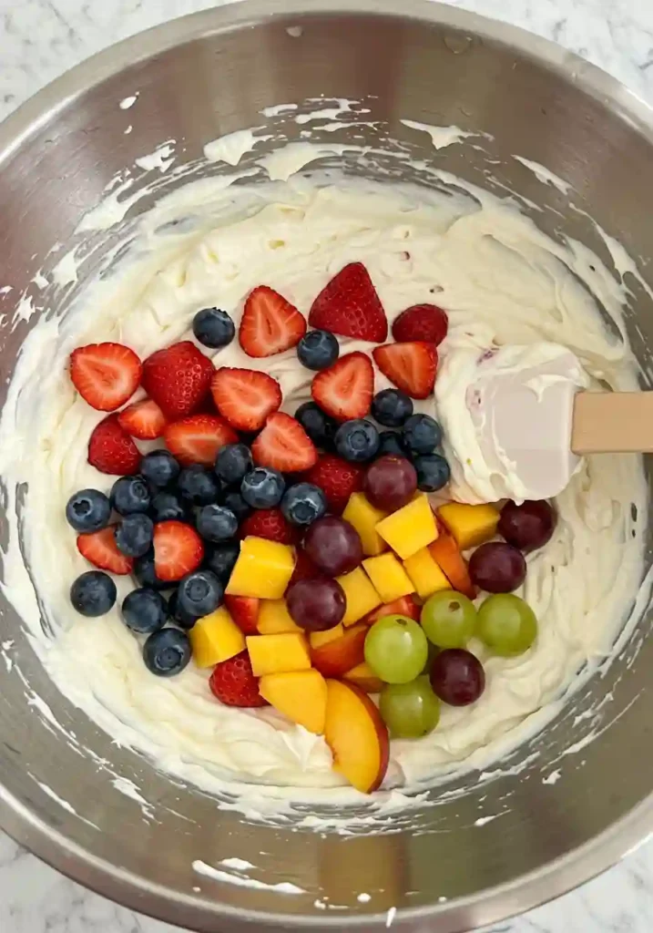 Fresh berries and sliced peaches being gently folded into the cheesecake fluff mixture