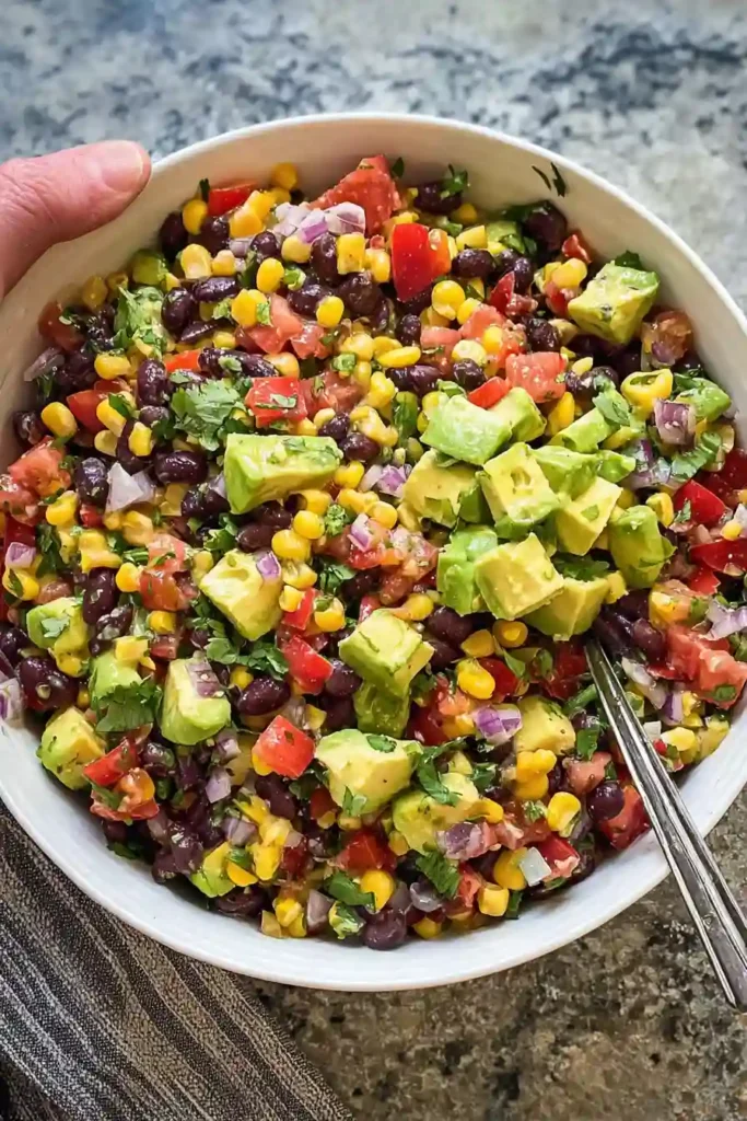 Chopped avocado being gently stirred into the black bean and corn salad