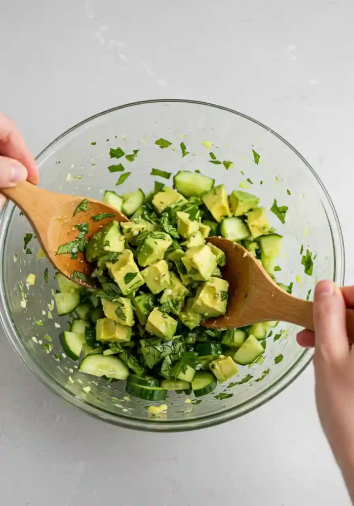 Mixing avocado, cucumber, and tomatoes with dressing in a bowl