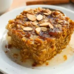 Freshly baked pumpkin oatmeal with golden brown top in white ceramic baking dish, garnished with cinnamon and served warm