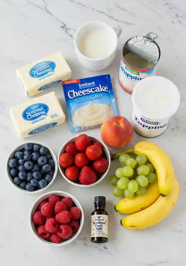 Assorted ingredients including cream cheese, pudding mix, whipped topping, and fresh fruits laid out on a kitchen counter