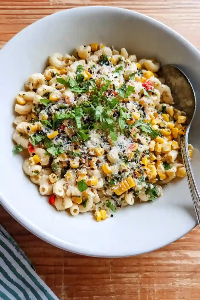 Hands mixing pasta, corn, and creamy dressing in a large bowl