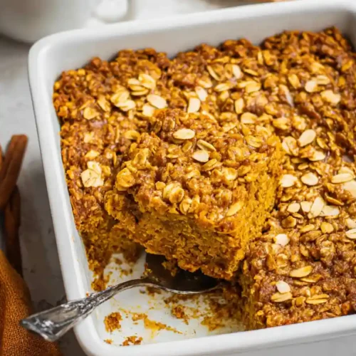 Golden pumpkin baked oatmeal cooling in baking dish on wooden cutting board, showing set texture and lightly browned surface