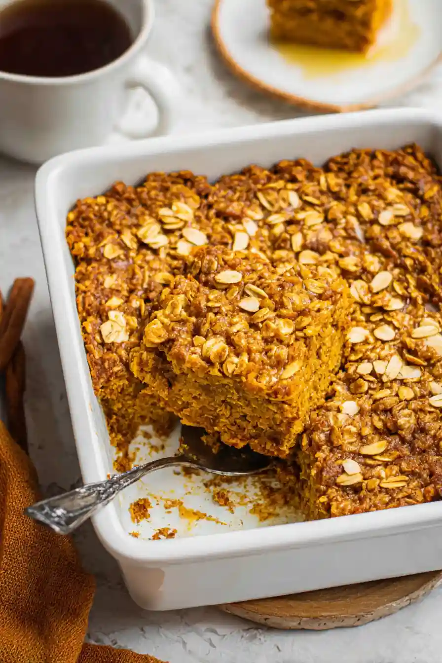 Golden pumpkin baked oatmeal cooling in baking dish on wooden cutting board, showing set texture and lightly browned surface