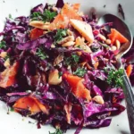Red Cabbage Salad with shredded purple cabbage, carrots, apples and pecans in white serving bowl with wooden spoons