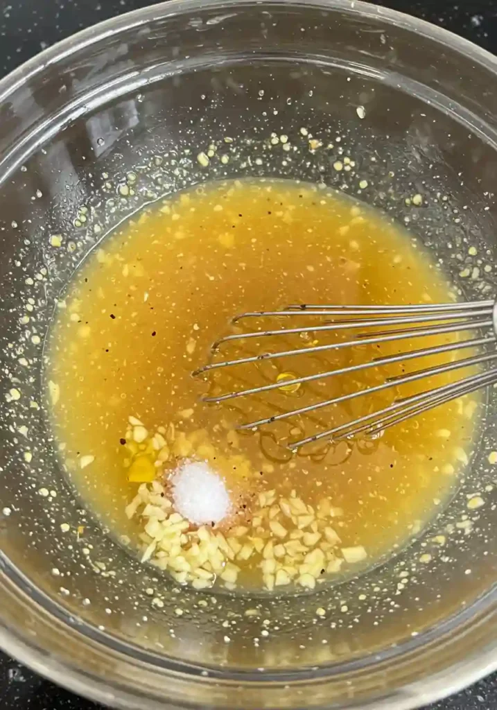 Hands whisking apple cider vinegar, olive oil, honey and Dijon mustard in glass bowl to make Red Cabbage Salad dressing