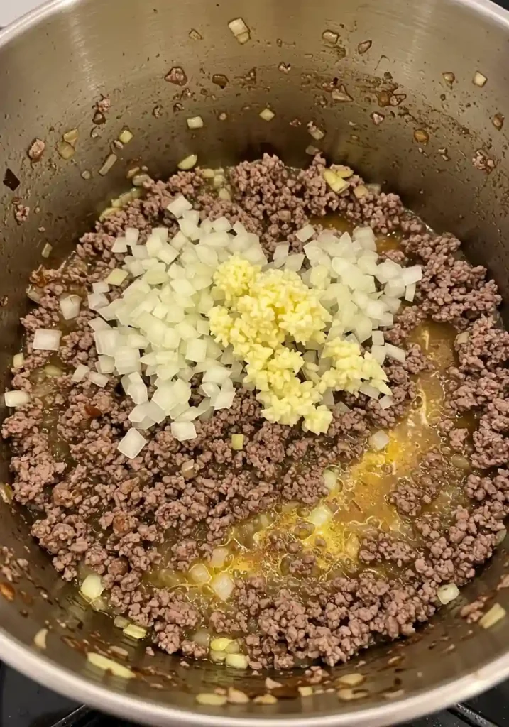Cooking diced onions and garlic with browned ground beef in a large Dutch oven pot