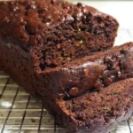 Sliced chocolate zucchini bread on wooden cutting board showing moist texture with chocolate chips