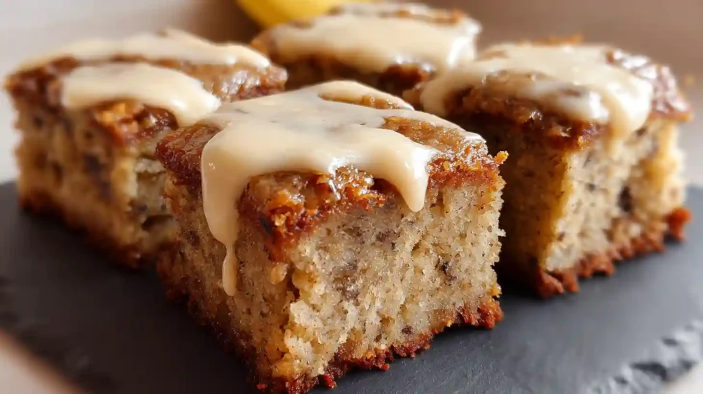 Frosted banana bread brownies cut into squares with one piece lifted to show moist interior texture
