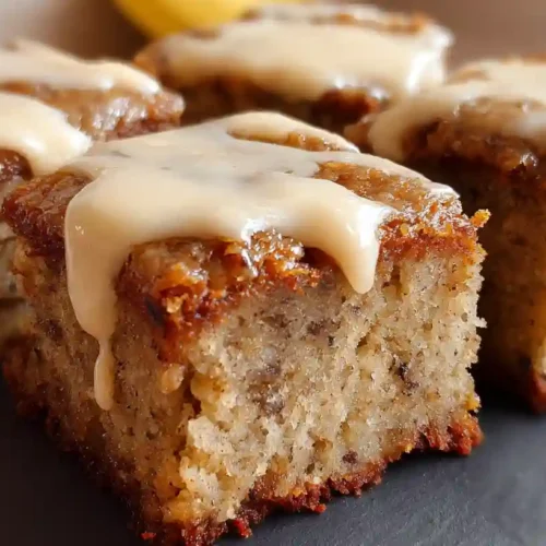 Frosted banana bread brownies cut into squares with one piece lifted to show moist interior texture
